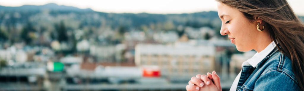 Woman praying with a city in the background, ready to change the world